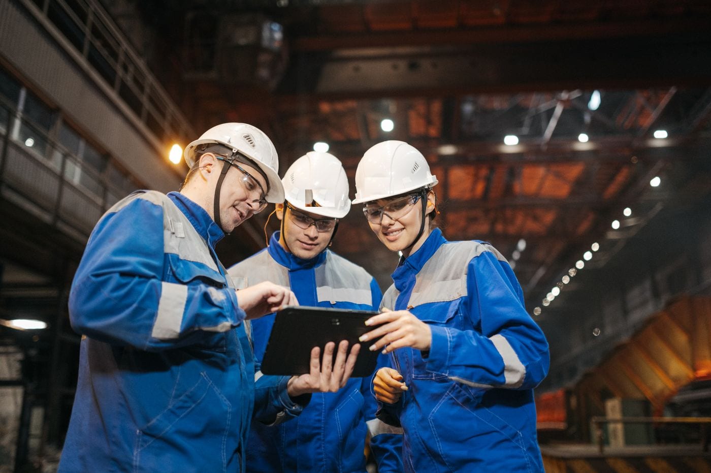 Workers in hard hats reviewing production data on a tablet in an industrial plant